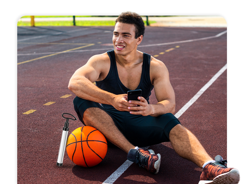 Athletic person sitting on outdoor basketball court with phone and basketball, wearing black tank top and shorts.