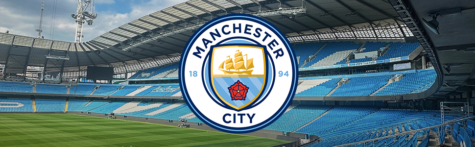Text reads 'MANCHESTER CITY'. Panoramic view of Manchester City's Etihad Stadium with team logo visible, showing empty blue seats and pitch under cloudy sky.