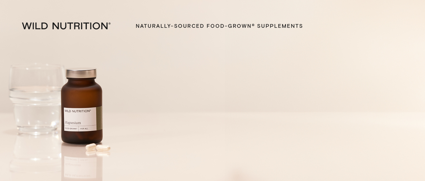 Brown glass supplement bottle with white label alongside clear glass of water on beige surface, with 'Wild Nutrition' branding visible above.