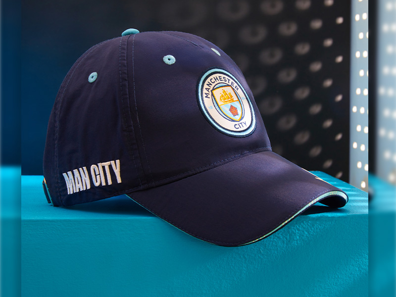 Navy blue baseball cap with Manchester City Football Club crest. 'Man City' text embroidered on side. Curved brim and adjustable strap visible.