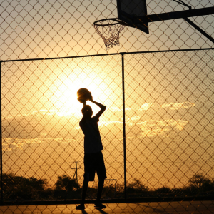 A basketball player shooting hoops as the sun is setting